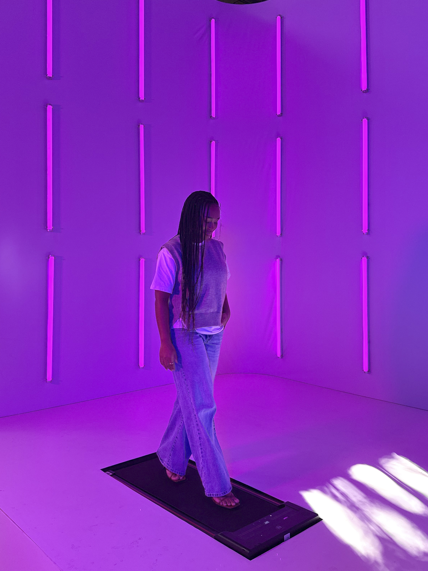 A creator walking a light-reactive runway in a room of vertical pink light tubes