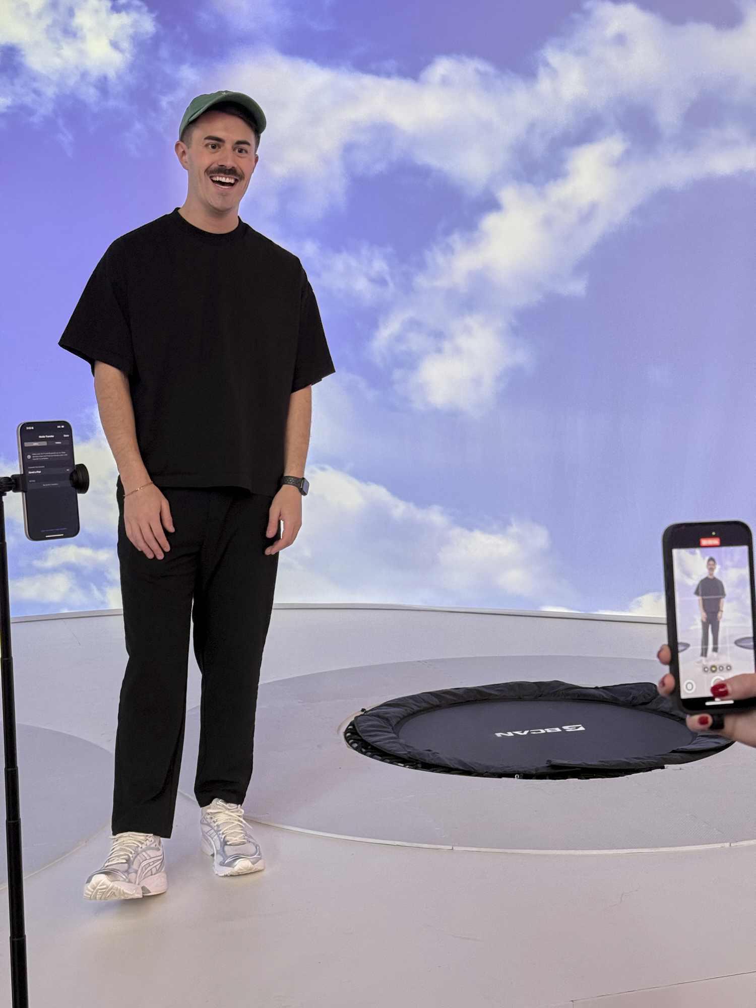 A creator being filmed on a trampoline set, sky scene on the projection wall behind
