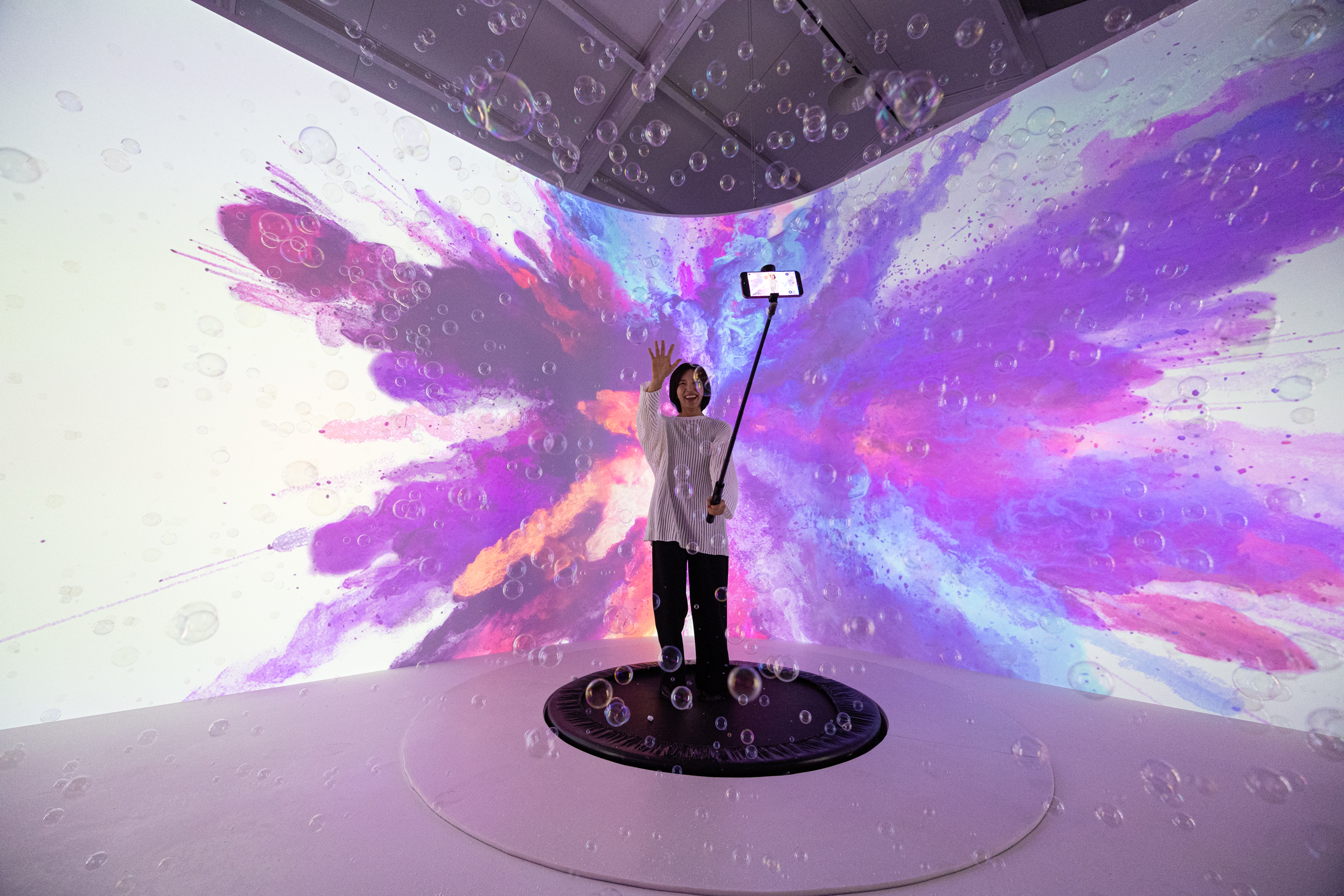 A creator waving on the trampoline, bubbles drifting across the projection wall