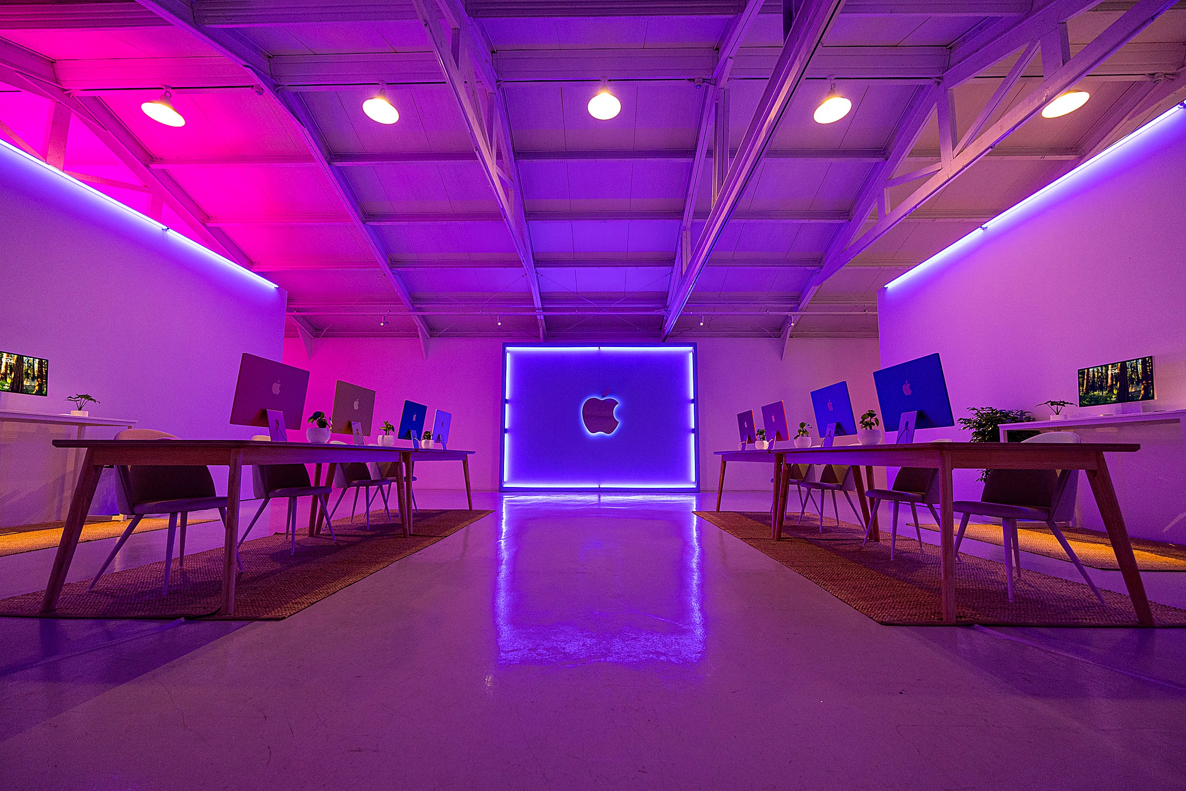 The workshop floor — product tables in coloured light facing an illuminated Apple logo wall